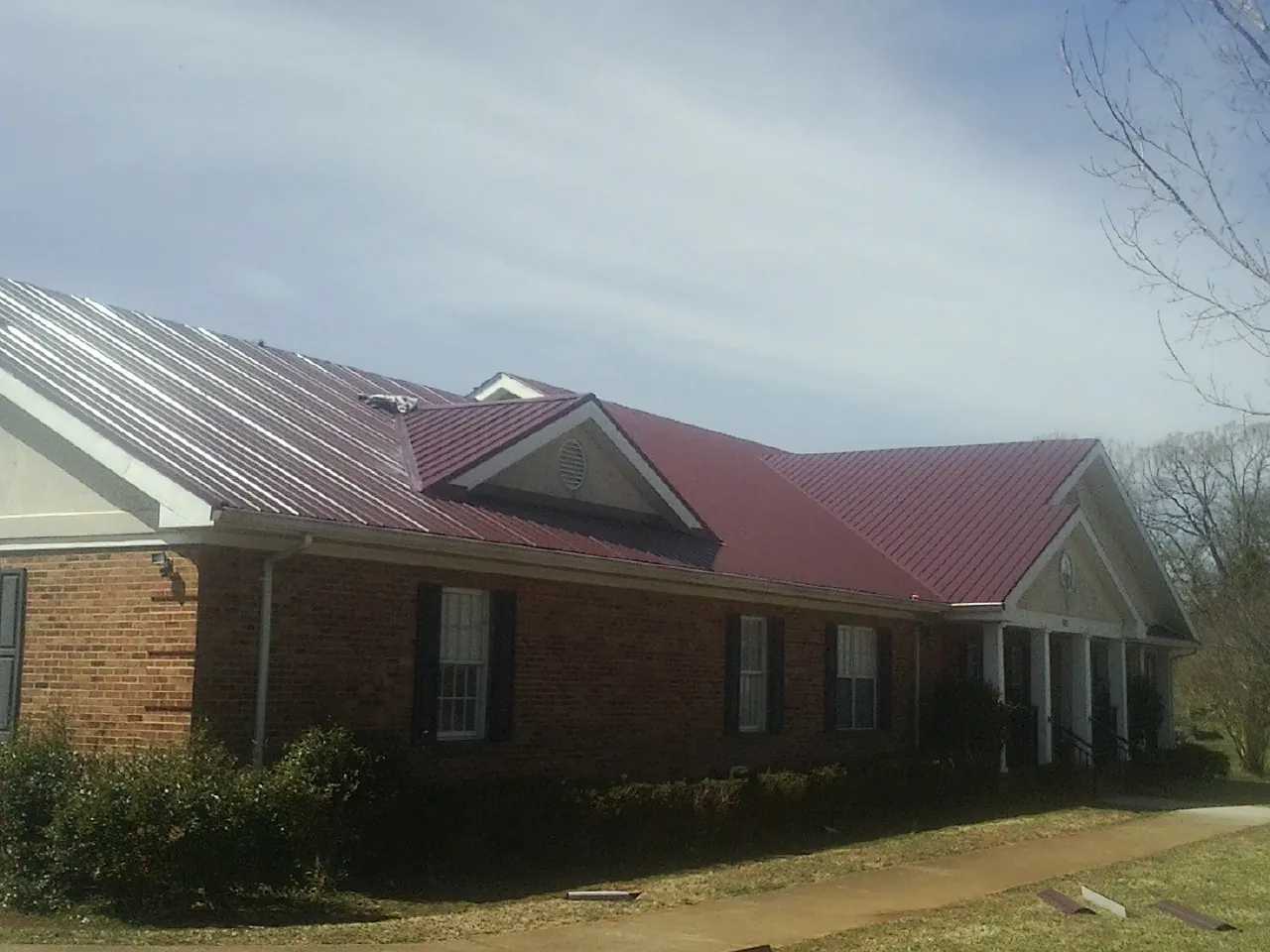 Red metal roof with gabled entries on a long brick building, from a Hail Damage Roof Repair job in Pataskala