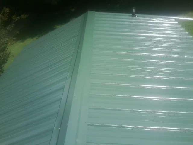 New green metal panels meeting at the ridge of a roof — Flat Roof Repair work by our crew in Pataskala