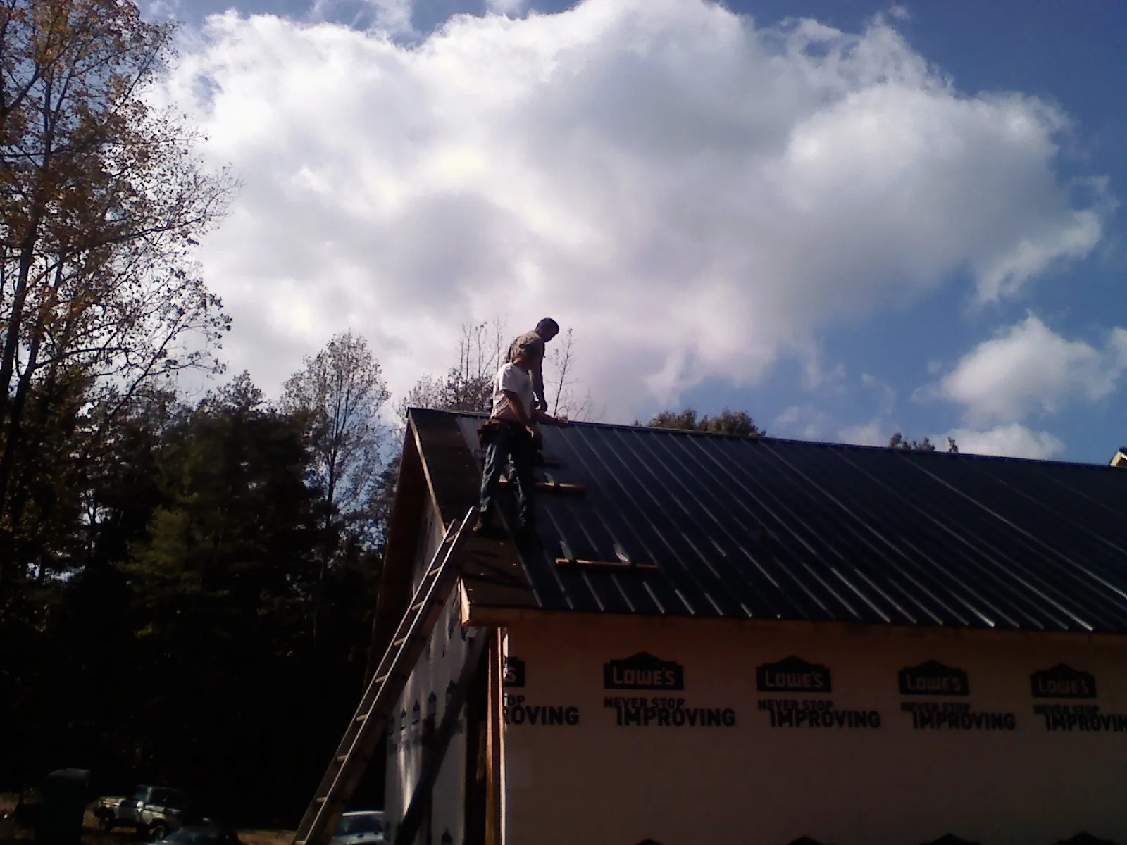 Roofer fastening dark metal panels high against a cloudy sky, from a Roof Inspection job in Pataskala
