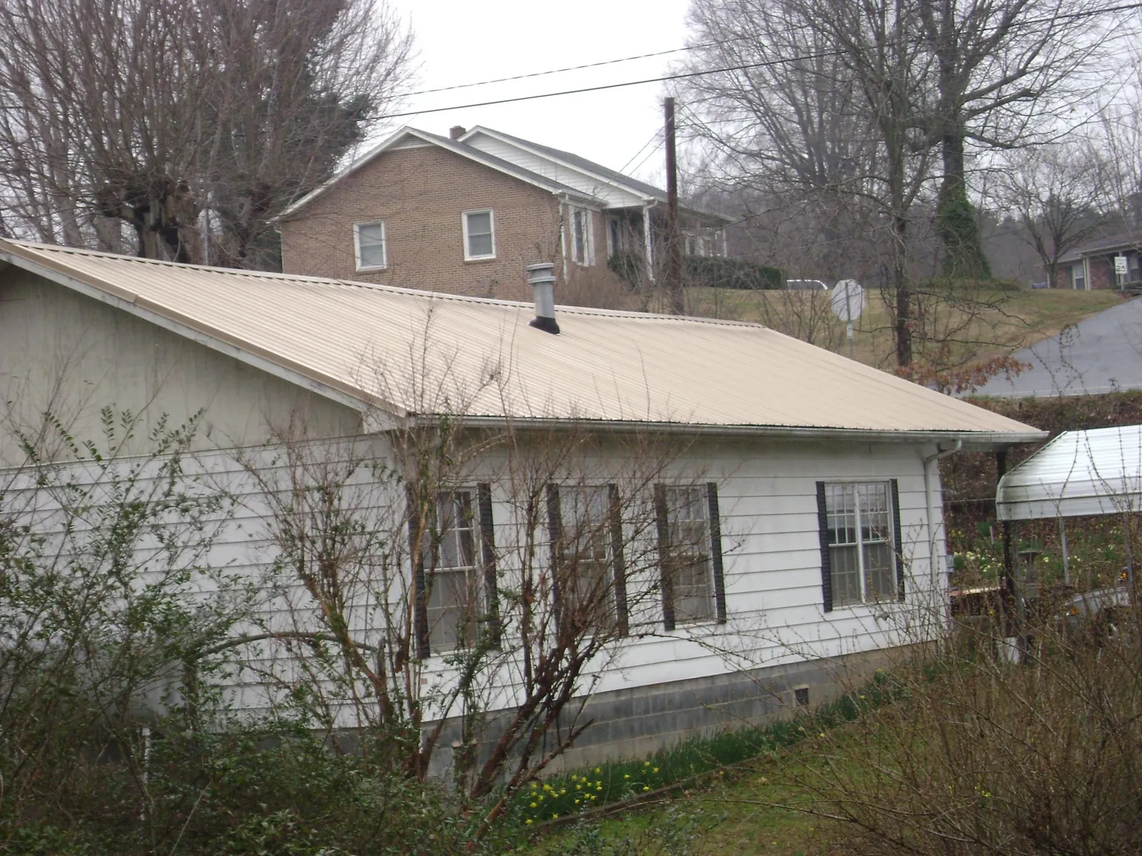 Tan metal roof on a white sided house set into a hillside — Commercial Roofing by Roofing Brothers in Pataskala